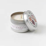 Pomegranate Travel Candle—soy wax, floral label, partially open tin lid on a white surface.