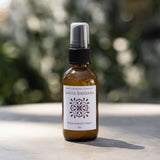 Amber bottle labeled Santa Barbara Room & Body Mist, clean scent on a sunlit surface, background softly blurred.
