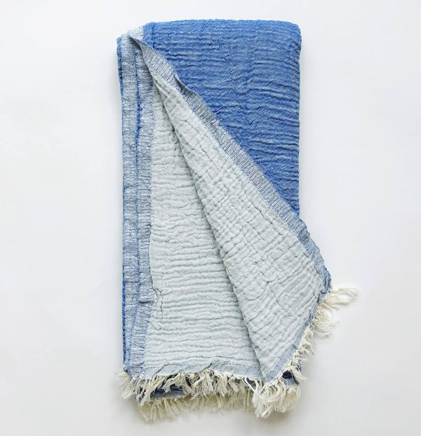 A cotton muslin towel in a rich blue color with a white fringe.