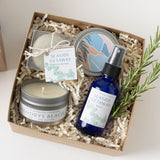 Seaside Getaway Spa Gift Box: includes candle, bath bomb, spray mist, tin, and rosemary sprig on white background.
