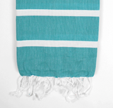 The Baby Hammam Towel in teal features two wide horizontal white stripes and short, frayed tassels at the bottom edge, shown against a plain white background.