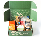 The California Crafted Treats Gift Box in a custom logo box features assorted snacks—orange, lime & sea salt almonds, organic pistachios, biscotti, and a granola bar—in a sustainable floral gift box with uplifting words on the lid.