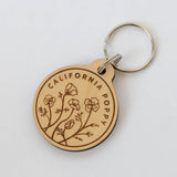 The California Poppy Wood Keychain features sustainably harvested wood, engraved with "California Poppy" and illustrated poppy flowers, and is attached to a metal keyring. Shown on a white background.
