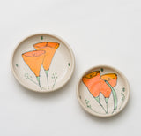 Two Ceramic Poppy Plates on a white background, each displaying hand-painted orange California poppies with green stems and leaves. The larger plate is on the left; the smaller one is on the right.
