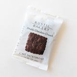 A white packet of Chocolate Cacao Nib Shortbread Cookie shows a square chocolate cookie on the front. Made with rich cacao nibs, it weighs 0.7 oz (20 g), and the best by date is printed on the side.