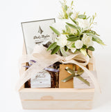 The Chocolate Gift Box features a chocolate bar, a small bouquet of white flowers, gourmet caramels, a jar of almonds, and a gift box with a green ribbon.
