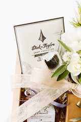 The Chocolate Gift Box includes Dick Taylor craft chocolate, handmade chocolate truffles in a paper cup, a ribboned jar, cream flowers, and a pale pink bow.