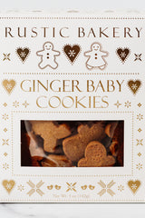 A box of Ginger Baby Cookies, decorated with gold gingerbread men and hearts. A window displays charming ginger cookies shaped like little people inside. Net weight: 5 oz (142g).