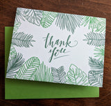 The Green Leaf Thank You Cards feature letterpressed green leafy designs and "thank you" in elegant script, paired with a matching green envelope on a wooden surface.
