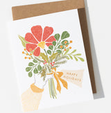 The Happy Holidays Bouquet Card Boxed Set features a USA-made card with a hand holding red flowers, berries, and green leaves beneath a "HAPPY HOLIDAYS" ribbon. Includes a brown envelope—perfect for your holiday card collection!.