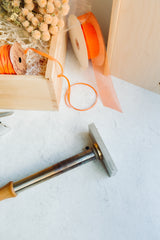 A Honey Wood Box Brand wooden box filled with dried flowers and orange ribbon sits on a light surface, alongside a metal tool with wooden handle, orange ribbon roll, translucent tulle, and a brand application fee note.