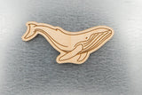 The Humpback Whale Wood Magnet, crafted from sustainably harvested wood and laser engraved with precision, is displayed on a gray textured surface.