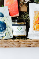 The Light Afternoon Treats gift basket features Artichoke Parmesan Tapenade, sourdough flatbread, and handcrafted chocolate truffles, all beautifully arranged on shredded green paper—the perfect afternoon snack.