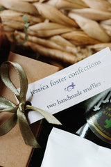 A close-up of a gift tag reading "Light Afternoon Treats," tied with a gold ribbon to a brown box, with other gluten-free gift items and a woven basket in the background.