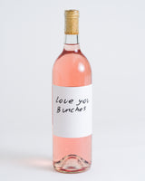 A clear glass bottle of Love You Bunches Rosé Natural Wine with a cork and a white label in handwritten black font, photographed on a plain white background—an inviting natural wine.