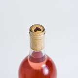 A bottle of Love You Bunches Rosé Natural Wine stands against a plain white background, featuring a cork in the neck and a heart-shaped mark on top.