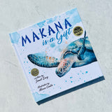 The children's book “Makana is a Gift: A Little Green Sea Turtle's Quest for Identity and Purpose” by Janet Lucy, illustrated by Alexis Cantu, features an illustrated sea turtle from Turtle Cove on the cover and lies on a light surface.