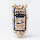 A clear plastic bag of Onion Garlic Santa Barbara Organic Pistachios - 3 oz shows the pistachios inside, with a front label displaying garlic illustrations and product details.