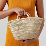 A person in an orange dress holds the Petite Market Basket (POS) with short handles against a plain background.