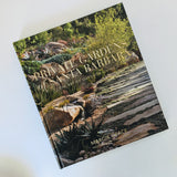 The hardcover "Private Gardens of Santa Barbara: The Art of Outdoor Living" is displayed on a white surface, featuring a cover image of a vibrant garden pathway edged with lush plants and trees.