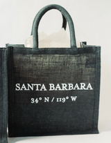 The Santa Barbara Coordinates Jute Tote - Blue is an eco-friendly bag with short handles featuring “Santa Barbara 34° N / 119° W” in white letters on the front. White tissue paper is shown inside.