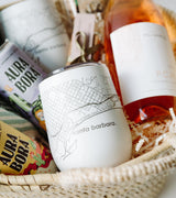 The Santa Barbara Wine Picnic Basket includes a white cup with a Santa Barbara map, two Aura Bora sparkling waters, rosé wine, and shredded paper filler—an ideal gift for any Santa Barbara lover.