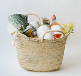 The Santa Barbara Wine Picnic Basket features a green patterned cloth, canned drinks, rosé wine, organic crackers, white decorative balls, and yellow flowers—an ideal beach picnic gift set displayed on a plain light background.