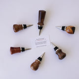 Six Santa Barbara Wood Wine Bottle Stoppers arranged in a circle around a business card on white background.
