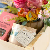A close-up of the Sweet Spring Gift Box, featuring a COAST agave + lemon soy candle, a vibrant fresh flower bouquet, and a pink Jack’s Treats box, all beautifully arranged in a wooden crate.