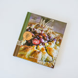 Wine Country Cookbook rests atop another book, showing a close-up of a rustic fruit dessert—an ideal companion for wine country cooking and delicious wine and food pairings.