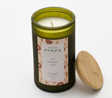 The Winter Poppy Candle features a green recycled glass jar, a white label with pine, bergamot, and ozone scents, and is made from plant-based soy wax. A wooden lid rests beside it on a white background.