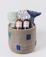Fair trade woven basket filled with baby bedtime accessories including bath products and a stuffed toy